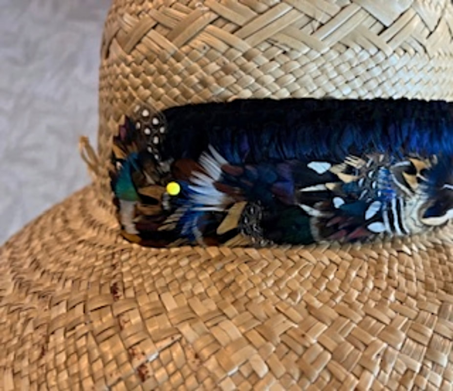 Handmade Hawaiian royalty hat band using feathers from Running Bug Farm. Hatband is shown partially complete on a woven tan hat.